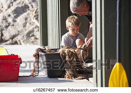 Stock Photo - Fisherman and boy removing fish from fishing net on pier. Fotosearch
