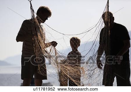 Stock Image - Fishermen and boy disentangling fishing net. Fotosearch