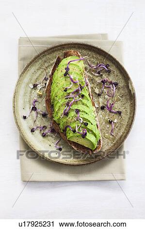 Stock Image - Fresh cut avocado on toasted bread with sprouts. Fotosearch