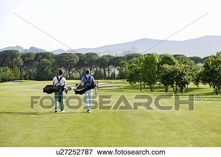 Stock Photo - Friends carrying golf bag walking on golf course. Fotosearch