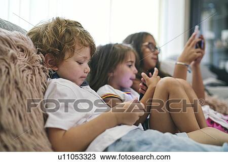 Stock Image - Friends enjoying computer games on sofa. Fotosearch