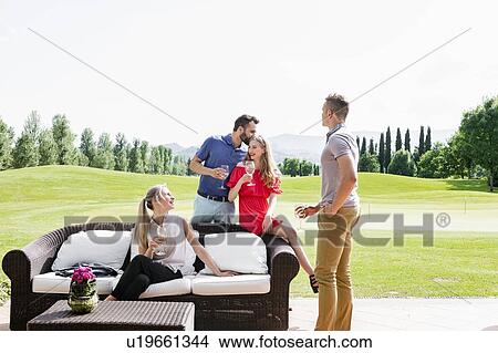 Friends enjoying wine and talking on sofa on golf course View Large Photo Image Picture - Friends enjoying wine and talking on sofa on golf course. Fotosearch