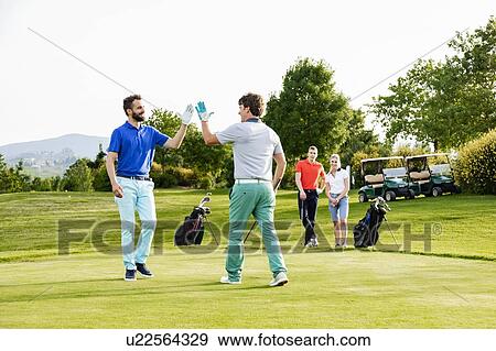 Stock Photo - Friends giving high five on golf course, couple watching in background. Fotosearch