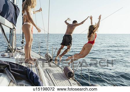 Stock Image - Friends jumping off sailboat into sea, Italy. Fotosearch