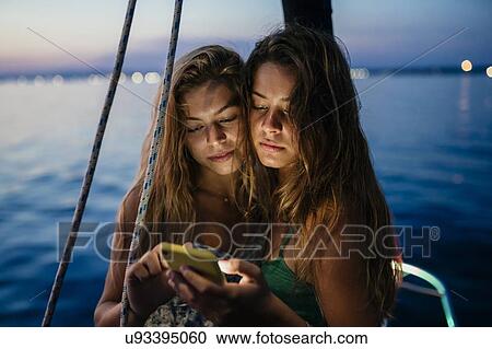 Stock Image - Friends on sailboat, sharing text message, Italy. Fotosearch