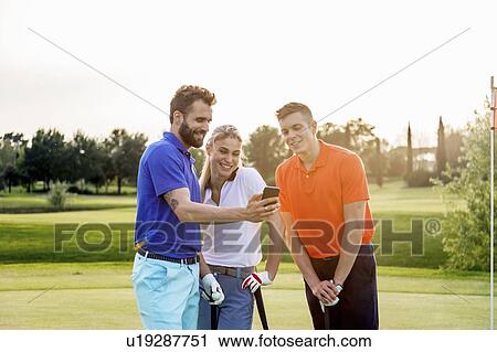 Stock Image - Friends reading text message in smartphone on golf course. Fotosearch