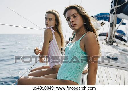 Stock Photo - Friends relaxing on deck edge of sailboat, Italy. Fotosearch