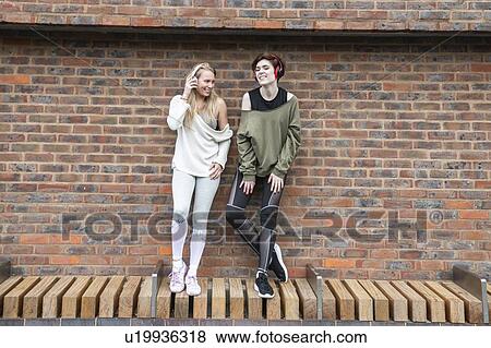 Friends relaxing, two girls listening to music on headphones on a street. View Large Photo Image Stock Photo - Friends relaxing, two girls listening to music on headphones on a street.. Fotosearch