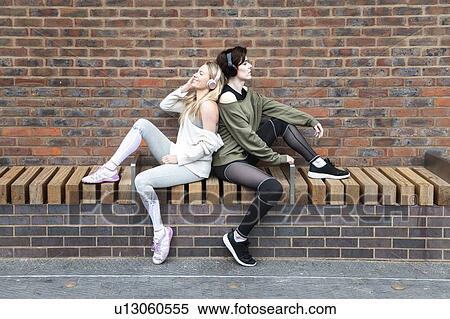 Friends relaxing, two girls listening to music on headphones on a street. View Large Photo Image Stock Photography - Friends relaxing, two girls listening to music on headphones on a street.. Fotosearch