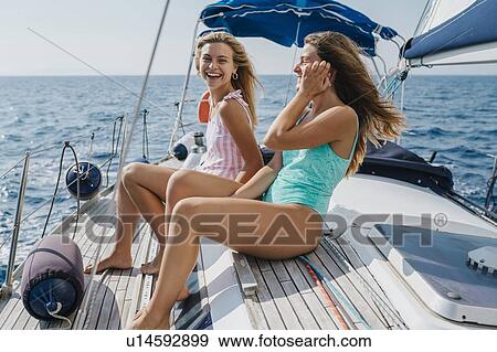 Stock Photo - Friends sitting on deck of sailboat enjoying sun and wind, Italy. Fotosearch