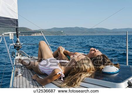 Stock Photo - Friends sunbathing on deck of sailboat, Italy. Fotosearch