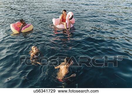 Stock Photo - Friends swimming and relaxing on floats on sea, Italy. Fotosearch