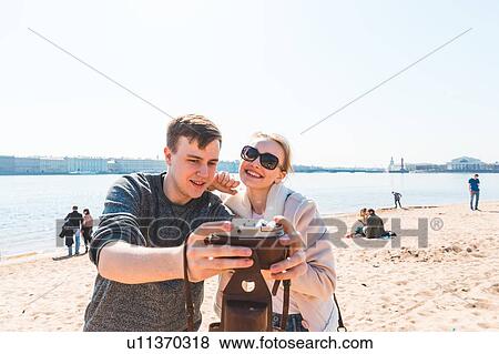 Stock Photo - Friends taking photograph on beach, Saint Petersburg, Russia. Fotosearch