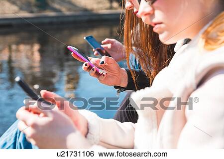 Stock Photograph - Friends using smartphone by river. Fotosearch