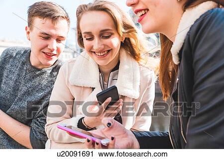 Stock Image - Friends using smartphone in city. Fotosearch