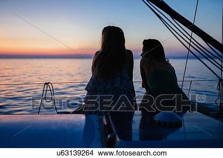 Picture - Friends watching sunset on sailboat, Italy. Fotosearch