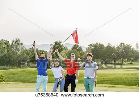 Stock Image - Friends waving flagstick on golf course. Fotosearch