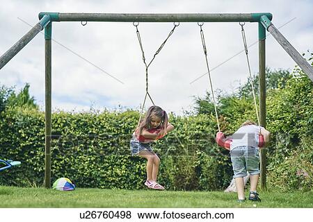 Stock Photo - Girl and boy twisting around on swings in garden. Fotosearch