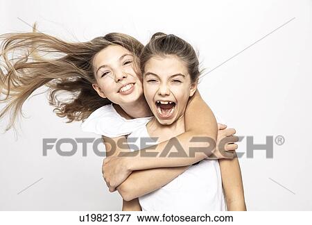 Stock Photo - Girl hugging sister from behind, white background. Fotosearch