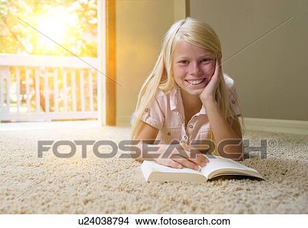 Picture - Girl lying on carpet, reading book. Fotosearch