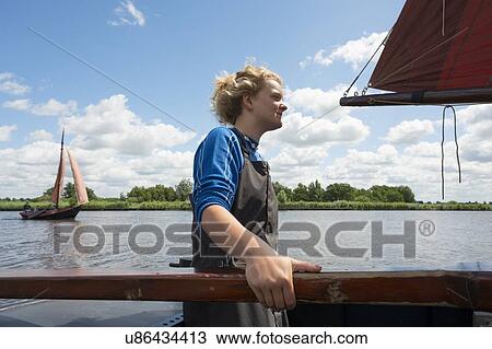 Stock Image - Girl stands at helm of large flat-bottom traditional sailing ship,. Fotosearch