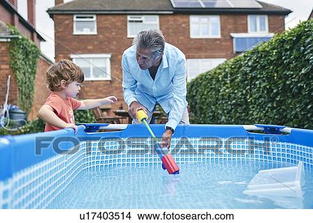 Picture - Grandfather helping boy fill up water gun from pool water. Fotosearch
