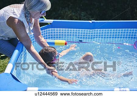 Stock Photo - Grandmother supporting granddaughter in pool. Fotosearch
