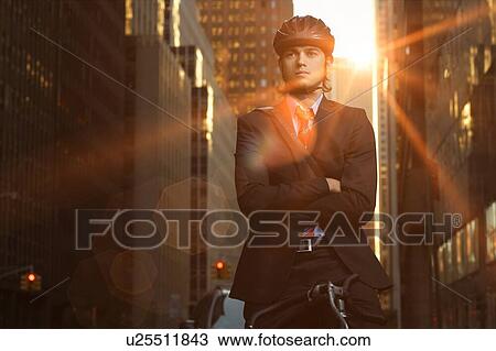 Stock Image - Handsome brunette business man commuting to work by bicycle wearing suit and tie. Fotosearch