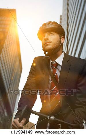 Stock Photo - Handsome brunette business man commuting to work by bicycle wearing suit and tie. Fotosearch