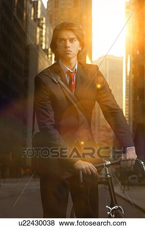 Stock Photo - Handsome brunette business man commuting to work by bicycle wearing suit and tie. Fotosearch