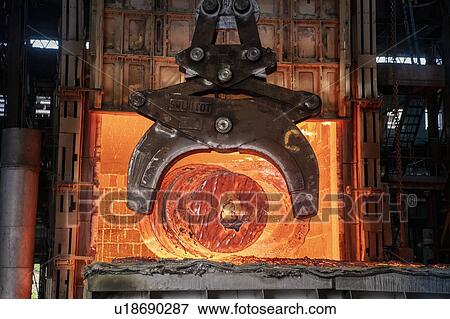 Stock Photo - Heat treated red hot steel ingot being lifted by crane in furnace in steelworks. Fotosearch