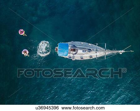 Stock Photograph - Holiday makers swimming off sailboat on sea, Italy. Fotosearch