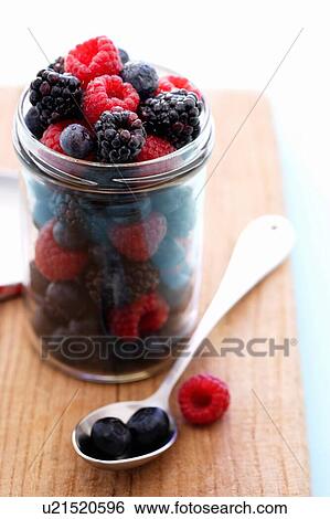 Stock Photograph - Jar full of raspberries, blackberries and blueberries on cutting board. Fotosearch