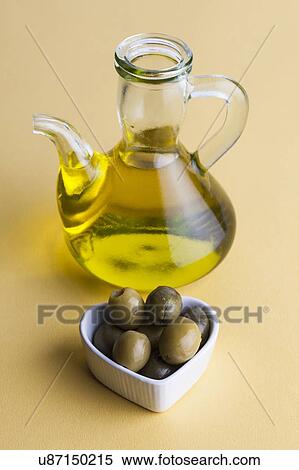 Stock Photography - Jug of olive oil with olives in heart shaped dish. Fotosearch