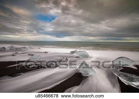 Stock Photo - Long shutter of white rushing over melting icebergs, Jokulsarlon beach, Iceland. Fotosearch