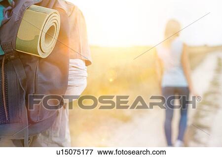 Stock Photo - Male hiker carrying backpack with woman walking in foreground on field. Fotosearch