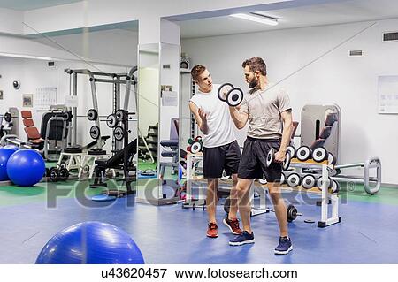 Stock Photo - Man coaching friend in gym. Fotosearch