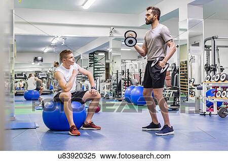 Stock Photography - Man coaching friend in gym. Fotosearch