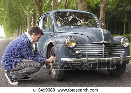 Man fixing tyre of vintage car on country road View Large Photo Image Stock Photo - Man fixing tyre of vintage car on country road. Fotosearch