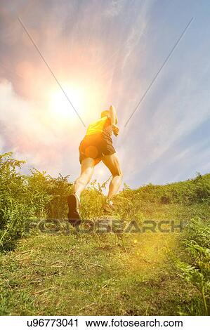 Stock Image - Man jogging in countryside, backview. Fotosearch