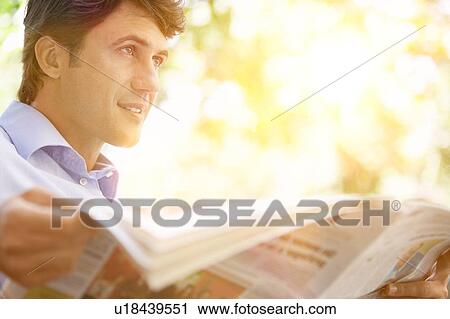 Stock Image - Man Reading Newspaper in sunny park. Fotosearch