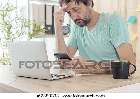Stock Image - Man receiving upsetting text message. Fotosearch