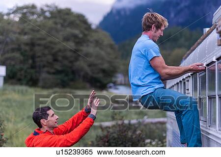 Stock Photography - Man watching back of friend climbing motorhome, Squamish, British Columbia, Canada. Fotosearch
