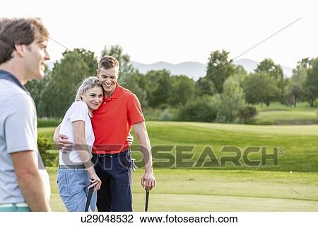 Stock Image - Man with couple hugging on golf course. Fotosearch