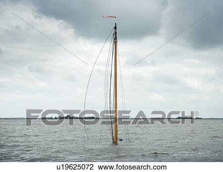 Stock Image - Mast of a sunken traditional flat-bottom sailing ship sticking up out of water.. Fotosearch