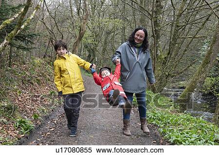 Stock Photography - Mother and sons walking together on a rainy misty day in woodland.. Fotosearch