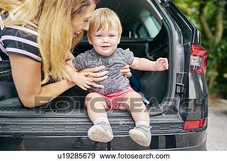 Stock Photo - Mother seating baby boy on back of vehicle. Fotosearch
