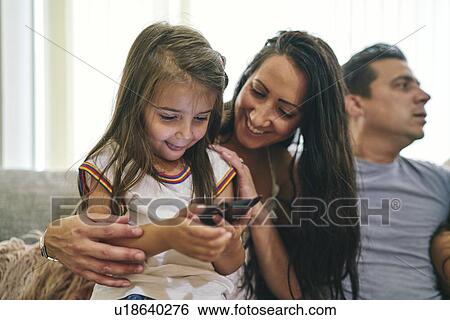 Mother watching daughter play computer game, father in background View Large Photo Image Stock Photograph - Mother watching daughter play computer game, father in background. Fotosearch