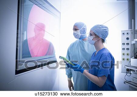 Stock Image - Nurse and surgeon inspecting screens in operating theatre in hospital setting. Fotosearch