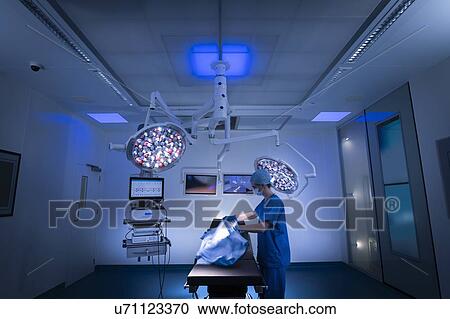 Stock Image - Nurse preparing darkened operating theatre in hospital setting. Fotosearch